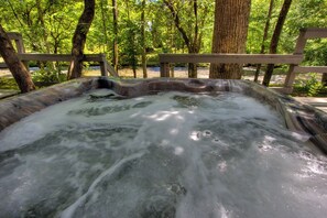 Een hottub omgeven door bomen en een houten terras.