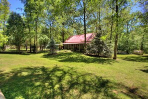 A cabin with a red roof surrounded by a grassy area and trees. - Creekside Cabin-Private Hot Tub-Firepit-Fishing (Cosby)