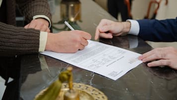 Eine Person unterschreibt ein Dokument an einem Tisch mit Marmorplatte.