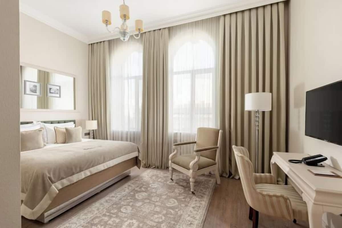 A hotel room with a bed, a desk, a chair, a TV, and a large window with curtains.