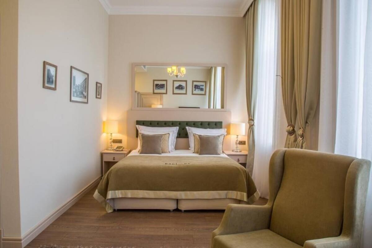 A hotel room with a large bed, two bedside tables with lamps, a chair, a mirror, and framed pictures on the wall.
