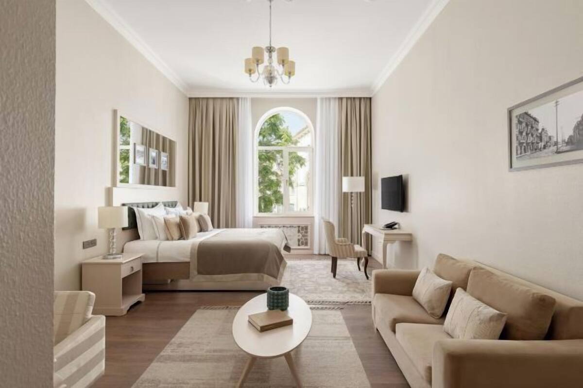 A hotel room with a bed, a sofa, a TV, a desk, and a window with curtains.