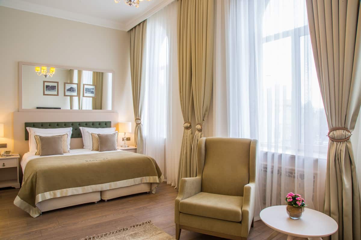 A hotel room with a large bed, a chair, a small table with flowers, and a mirror with pictures.
