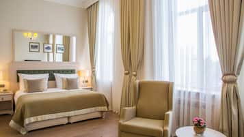 Habitación de hotel con una cama grande, una silla, una mesita con flores y un espejo con fotografías.