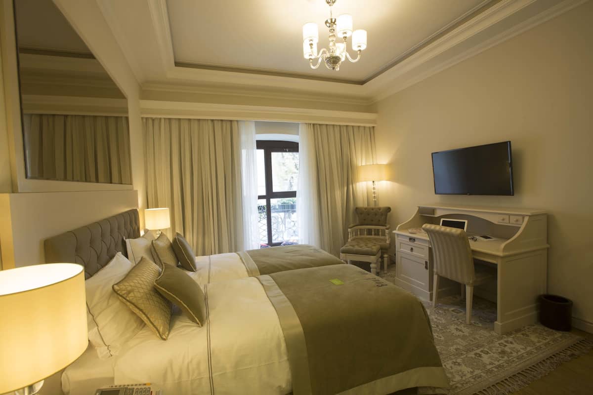 A hotel room with two beds, a desk, a chair, a television, and a window with curtains.