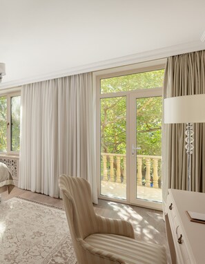 Ein Zimmer mit einer großen Glasschiebetür, die auf einen Balkon führt, einem gestreiften Sessel, einer weißen Lampe und einem Bett mit einem gemusterten Teppich.
