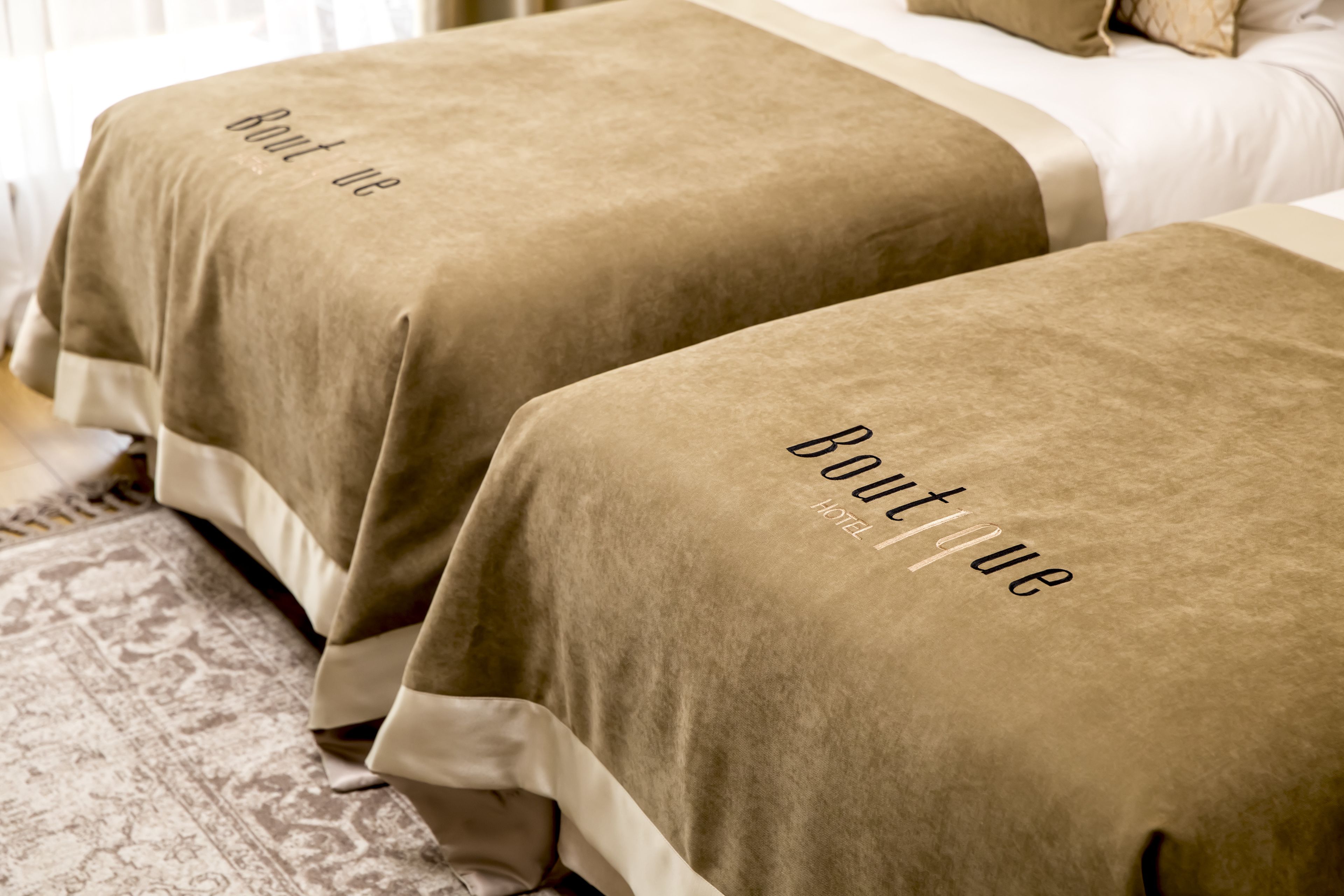 Zwei Betten mit beigefarbenen Decken, mit der Aufschrift 'Boutique Hotel'.