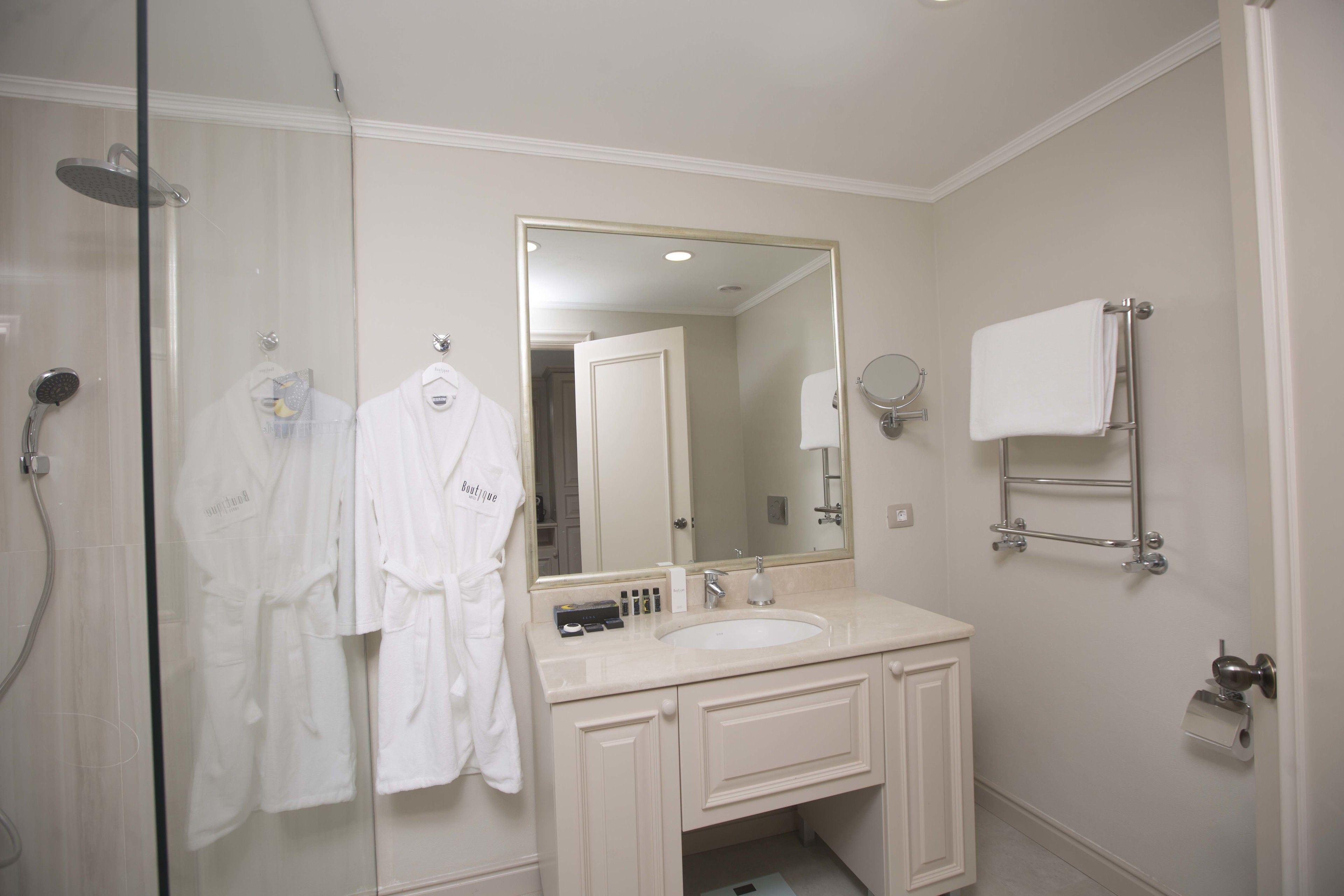 A bathroom with a glass shower enclosure, a sink with a mirror above it, and a towel rack on the wall.