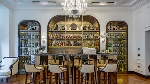 Zona de bar con barra central, varios taburetes y estantes llenos de botellas.