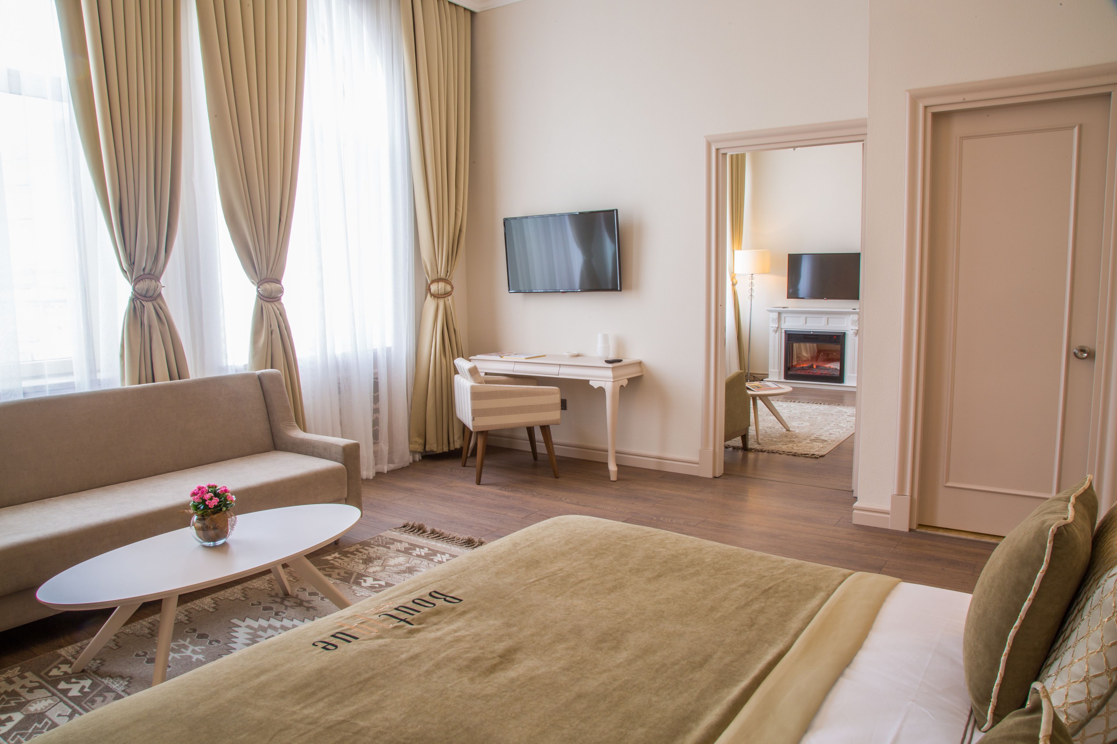 A hotel room with a bed, a sofa, a desk, a TV, and a fireplace.