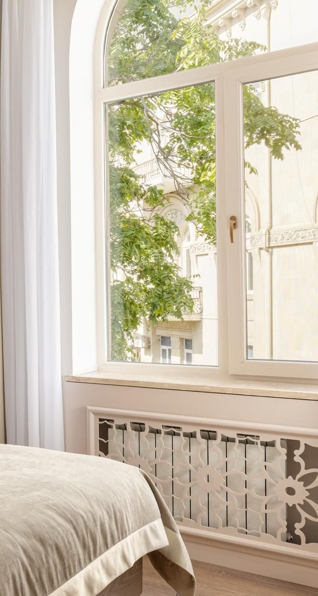 A bedroom with a large window, a radiator below, and a bed with a white bedspread.