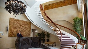 Un lobby espacioso con una recepción de mármol, un cuadro abstracto de gran tamaño, una escalera en espiral y plantas en macetas.