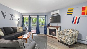 A living room with a sofa, armchair, fireplace, TV, and flags on the wall. - Pointes North Inn 109 | Downtown Charlevoix | Indoor pool (Charlevoix)