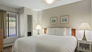 A neatly arranged bedroom with a large bed, two bedside lamps, a ceiling fan, and two framed pictures on the wall.
