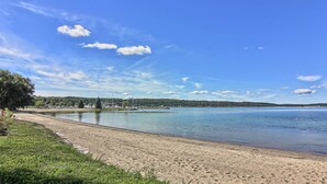 A beach with a clear view of the water, a sandy shore, and a distant shoreline with buildings and trees.
