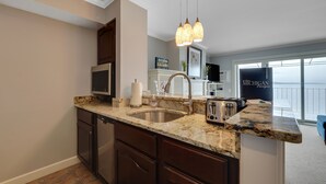 A kitchen with a granite countertop, stainless steel sink, and a toaster. There is a sign on the wall that says "Michigan" and a window with a view.