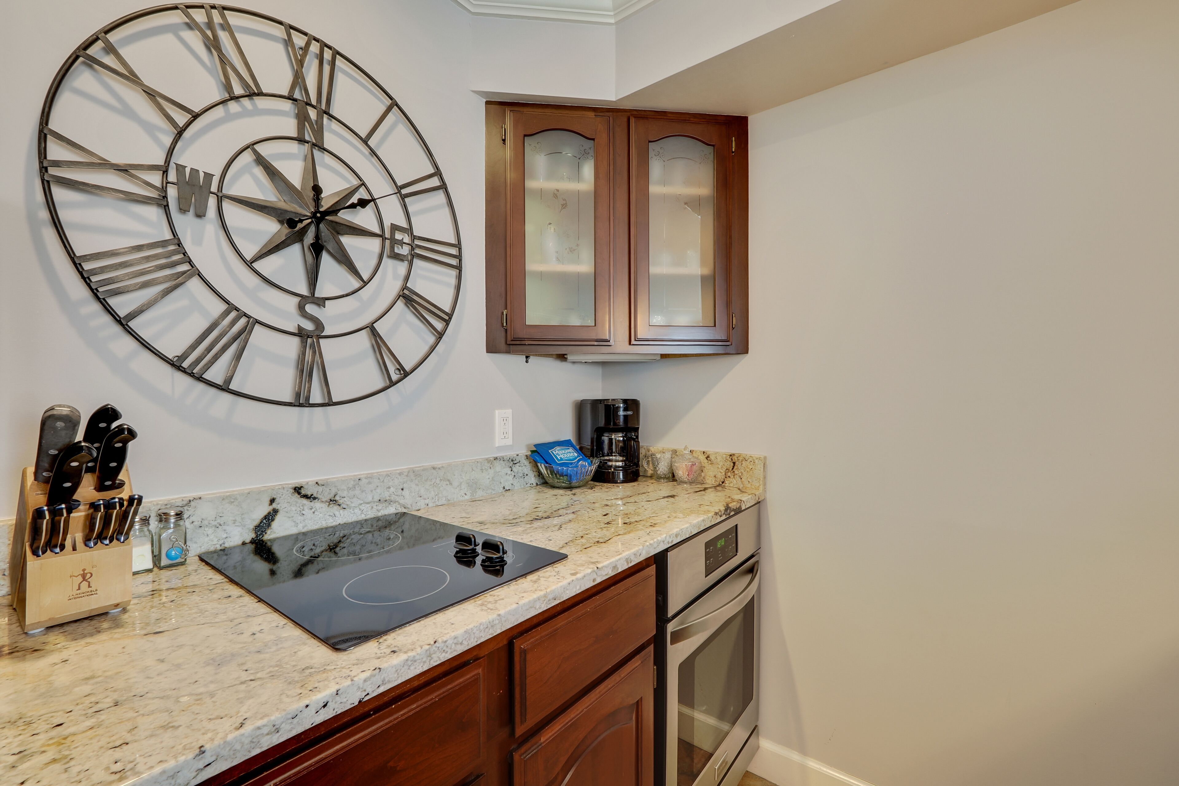 Una cocina con un reloj de pared grande, horno empotrado y cafetera.