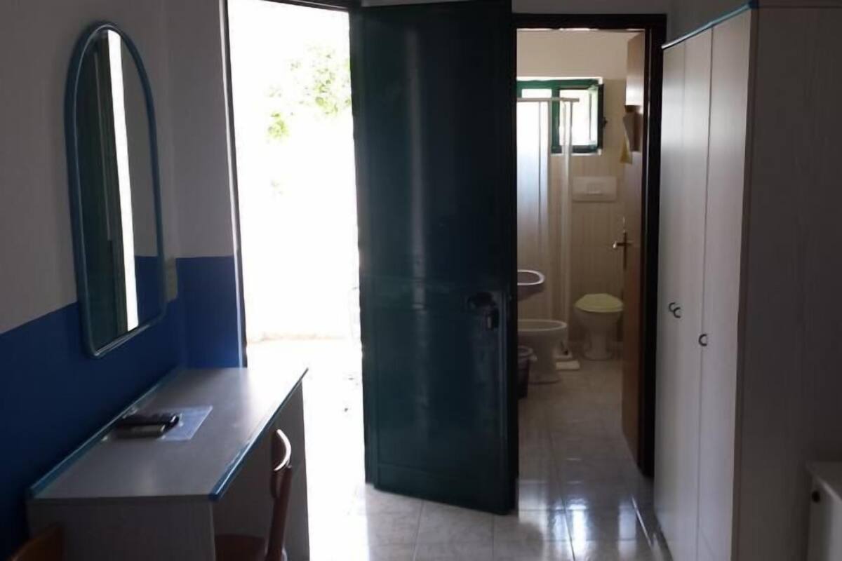 Une pièce comprenant un bureau, une chaise et une armoire. Une porte donne accès à une salle de bain équipée de toilettes et d’un lavabo.