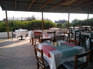 An outdoor patio with multiple tables and chairs, covered by a roof. - Villa Petrusa (Lipari)
