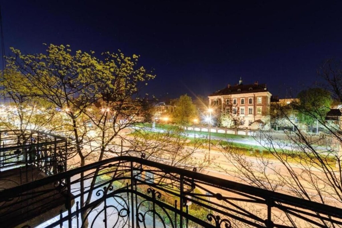 A night view of a building with a balcony, surrounded by trees and streetlights.