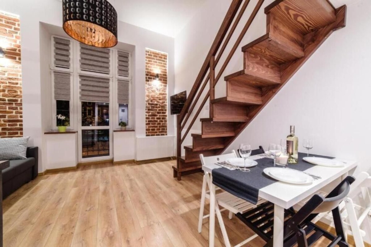 A dining area with a wooden staircase, a table set for two, and a brick wall.