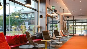 A modern waiting area with seating, tables, and large windows offering views of the outside.