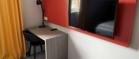 Habitación de hotel compacta con escritorio, silla y televisor montado.