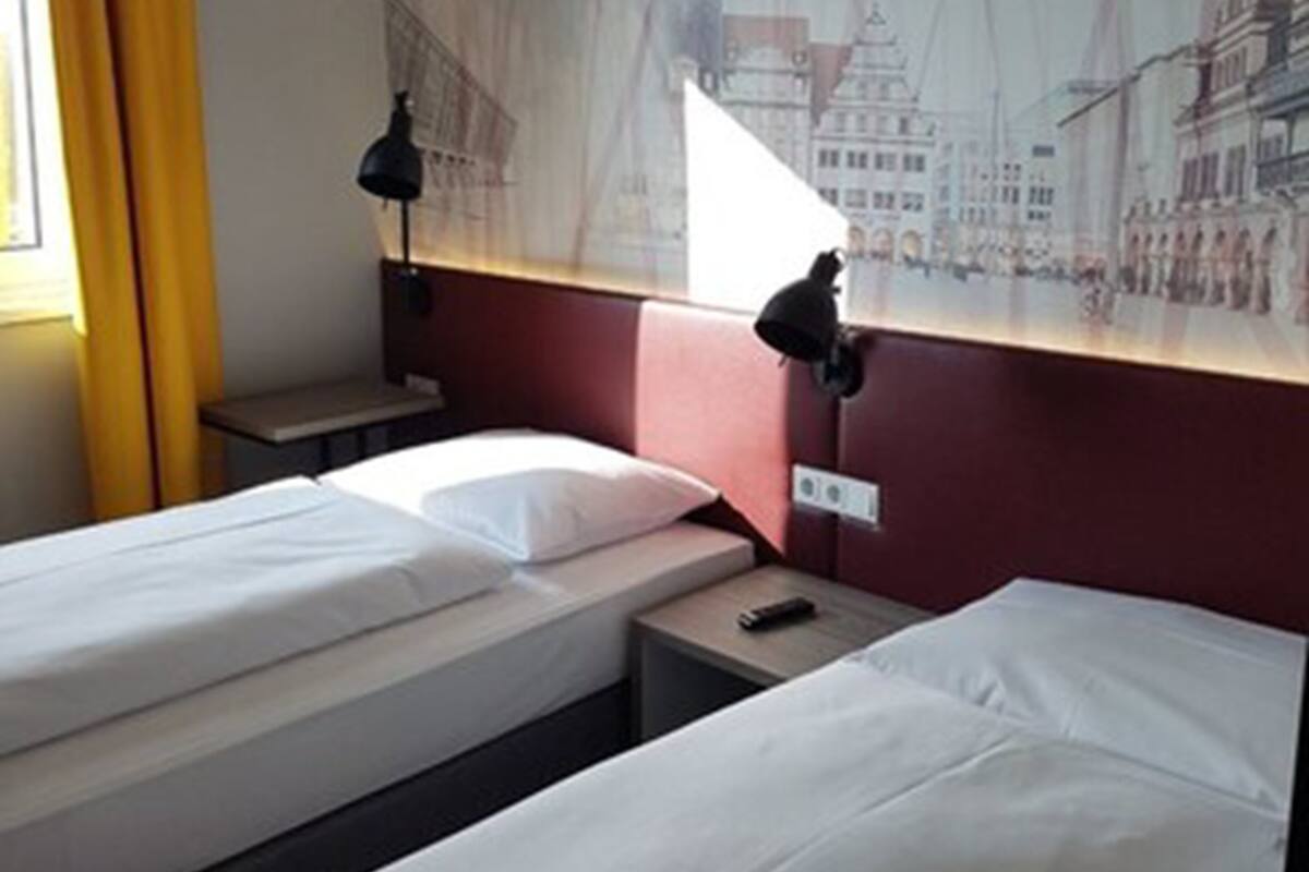 Ein Hotelzimmer mit zwei Einzelbetten, einem Nachttisch, einer Lampe und einem Wandbild.