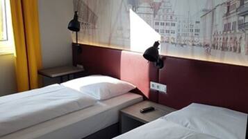 Una habitación de hotel con dos camas individuales, una mesita de noche, una lámpara y un mural en la pared.