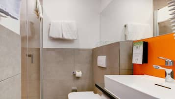 A modern bathroom with a glass shower enclosure, a white toilet, and an orange accent wall.