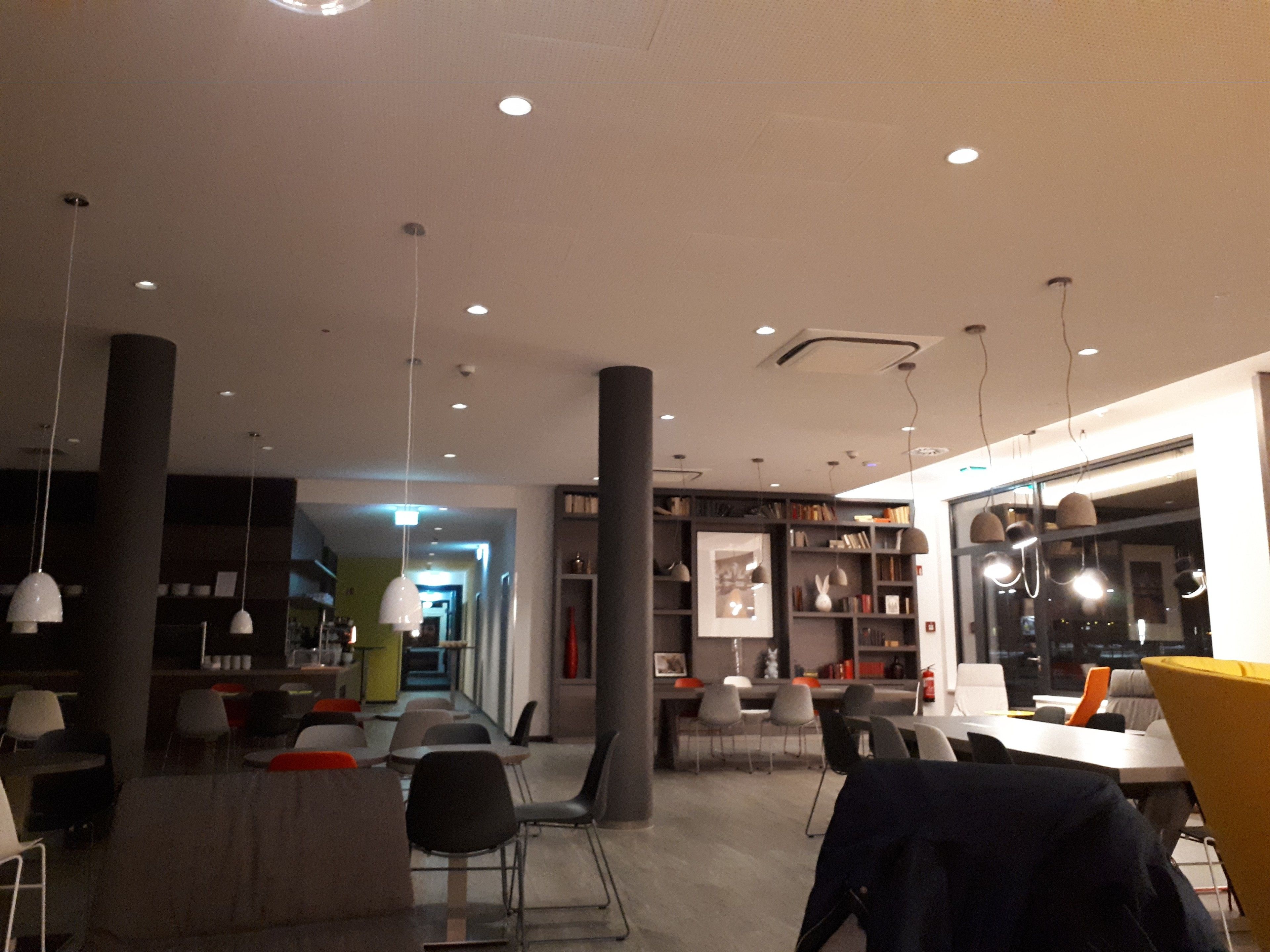 A modern interior with a long table and chairs, bookshelves, and pendant lighting.