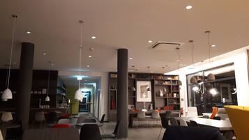 A modern interior with a long table and chairs, bookshelves, and pendant lighting.