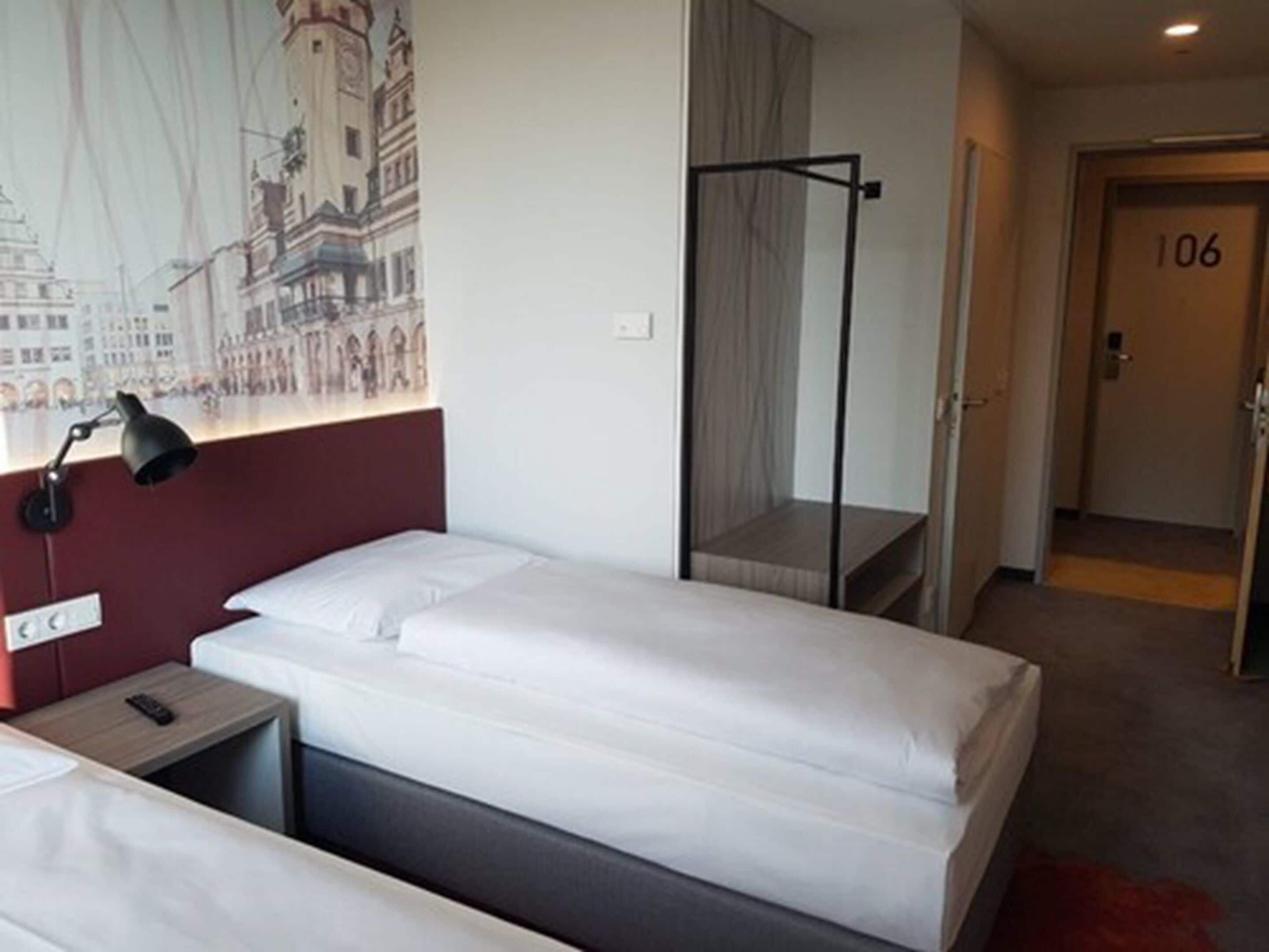 Een hotelkamer met twee bedden, een nachtkastje, een lamp, een spiegel en een deur met het nummer 106.