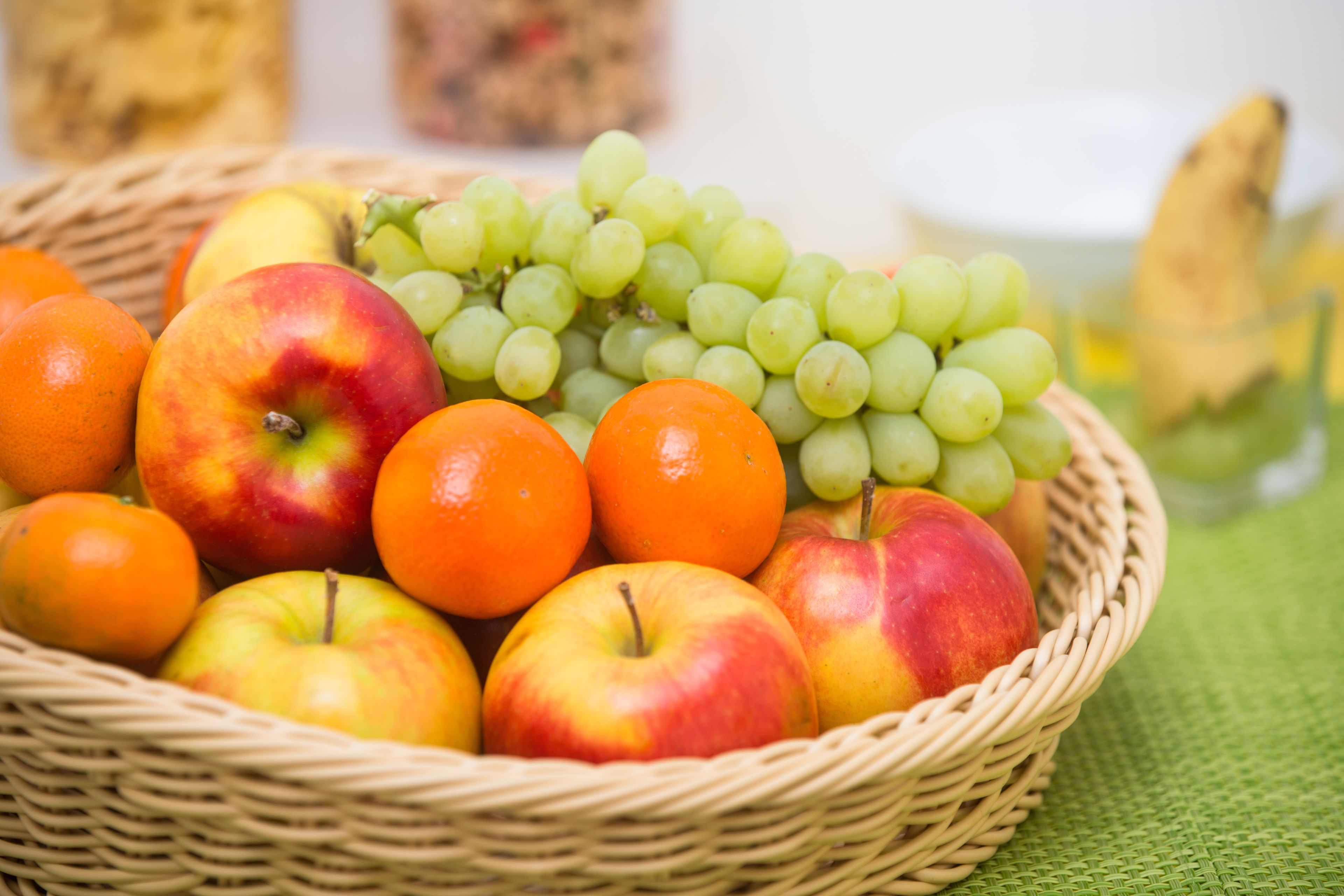 A wicker basket filled with apples, oranges, and green grapes.