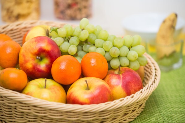 Una cesta de mimbre llena de manzanas, naranjas y uvas verdes.