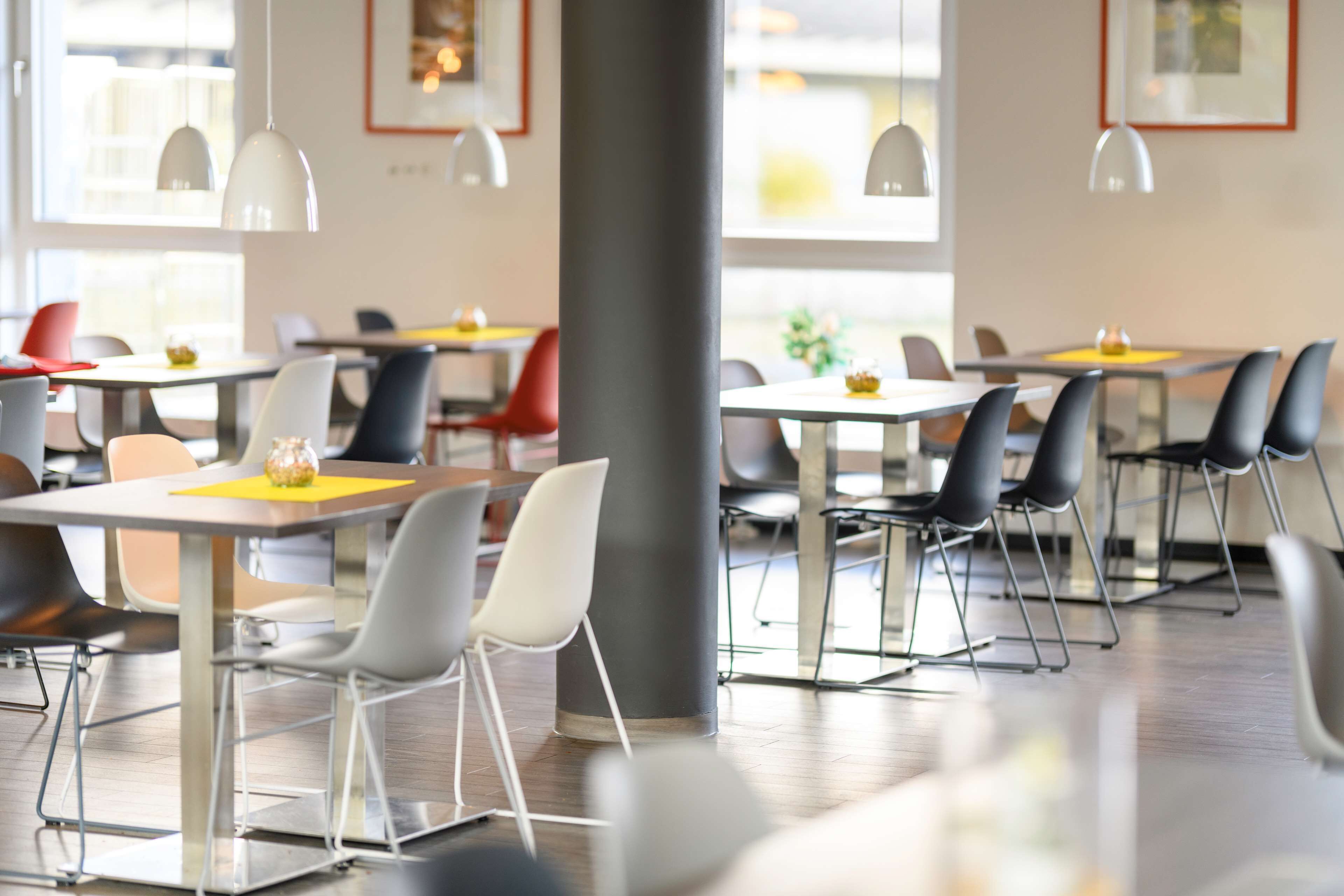 Un espace de restauration moderne, doté de tables et de chaises, de grandes fenêtres et de luminaires suspendus.
