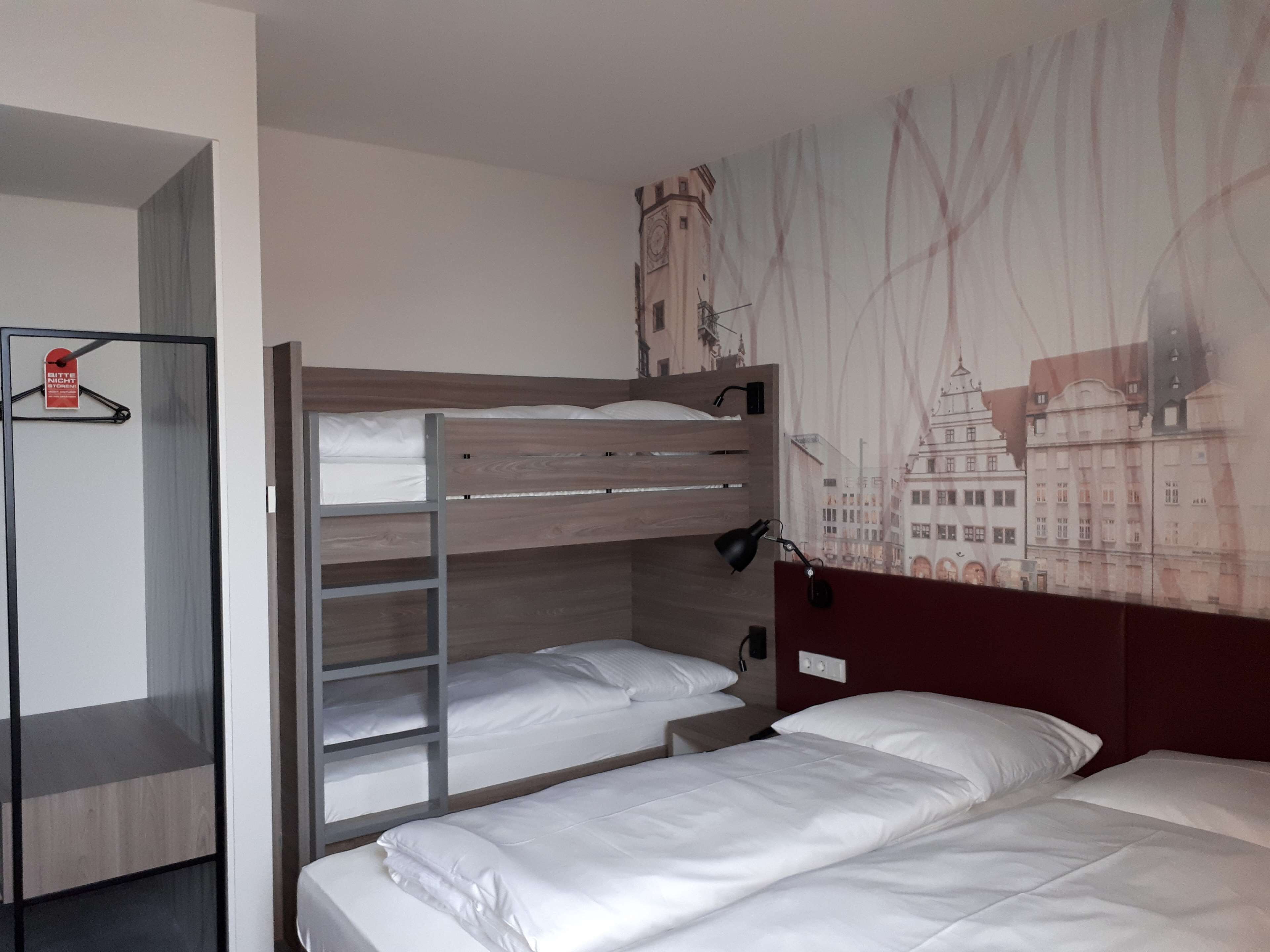 Ein Hotelzimmer mit Etagenbett, Schreibtisch und Wandgemälde mit Stadtansicht.