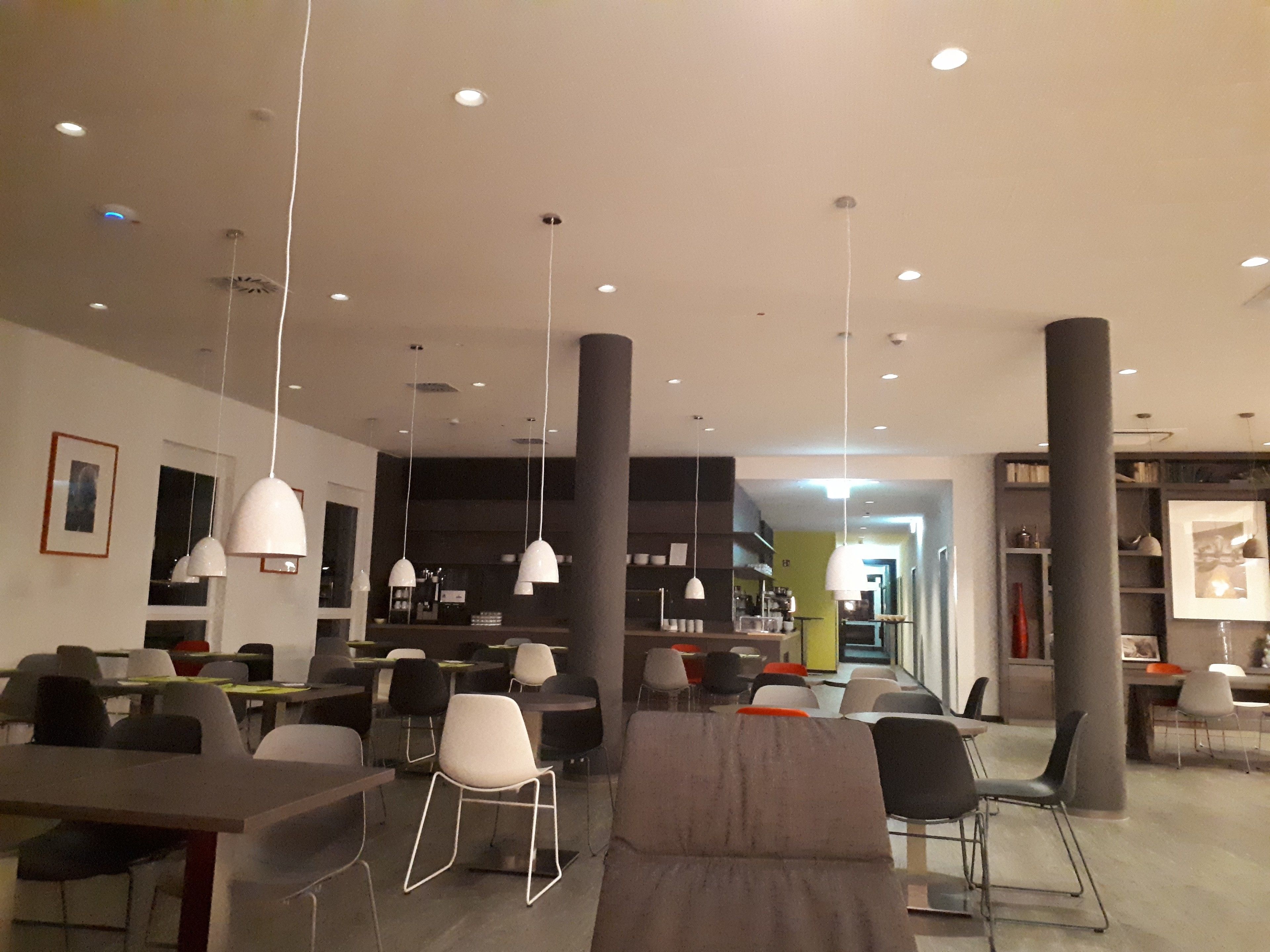 Un interior moderno con varias zonas de estar, iluminación colgante y una escalera visible que sube a otro nivel.
