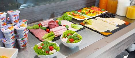 Un bufé con diversas opciones de comida, incluyendo ensaladas, carnes y fruta.