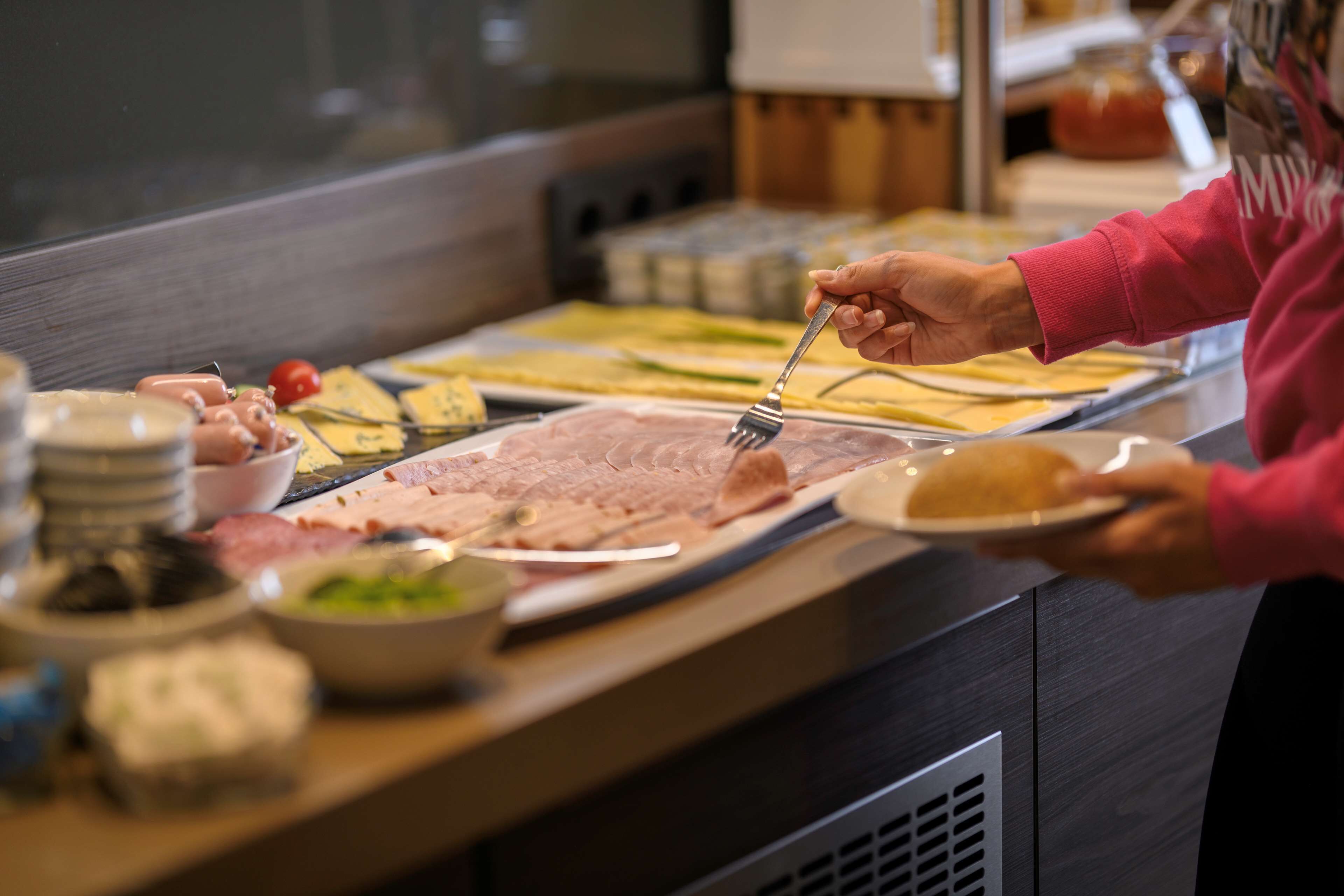 Montaje de bufé con diferentes alimentos y una persona servándose.
