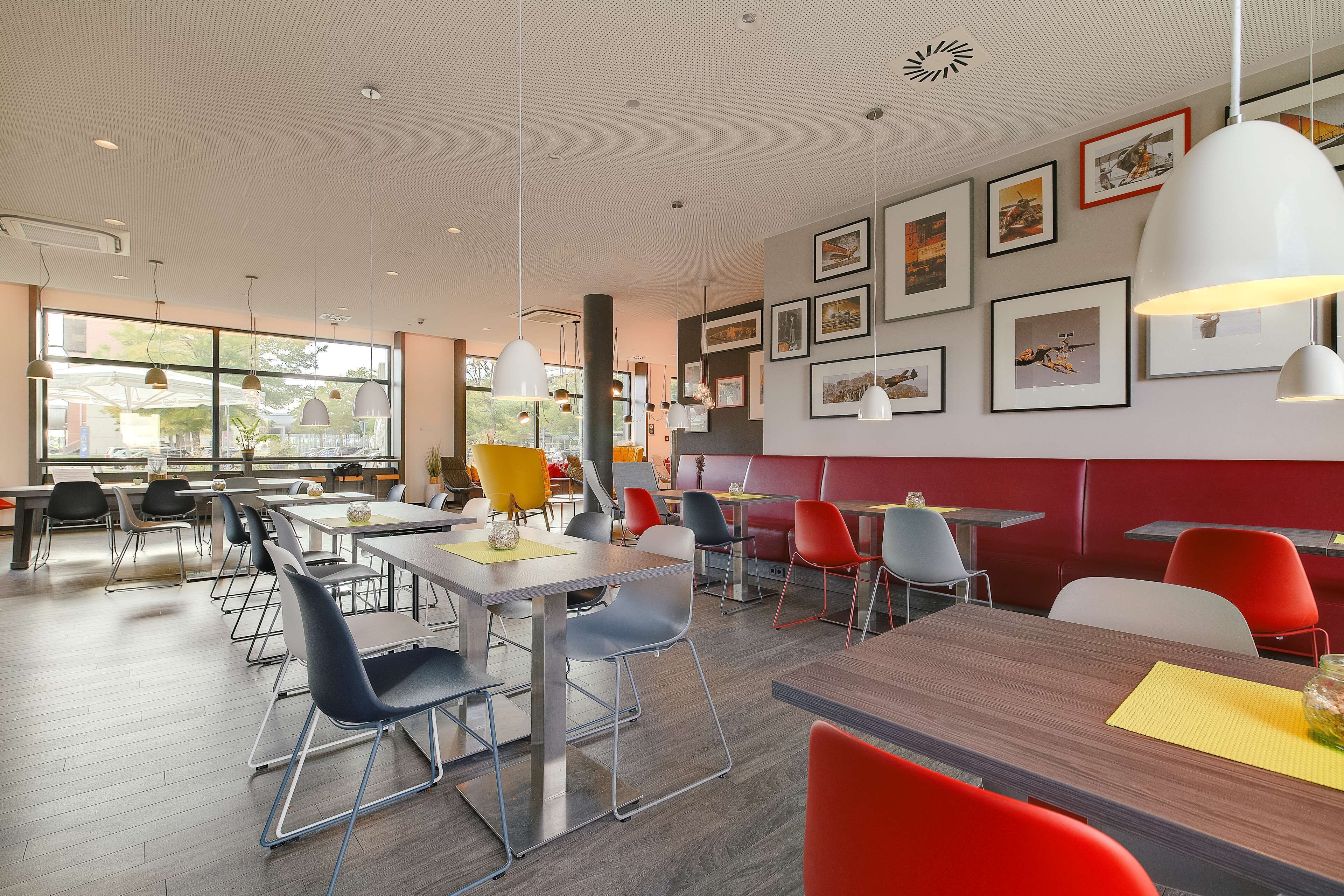 Un comedor moderno con mesas y sillas, ventanas amplias y obras de arte en las paredes.