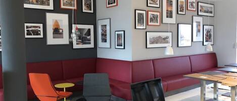 A modern lounge area with a red cushioned bench, a small table, and colorful chairs.