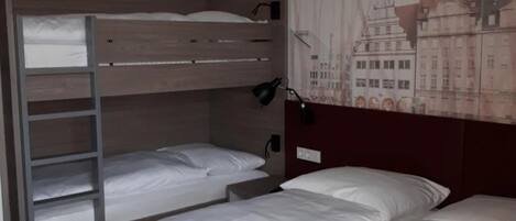A hotel room with two single beds, a bunk bed, a red carpet, and a cityscape mural on the wall.