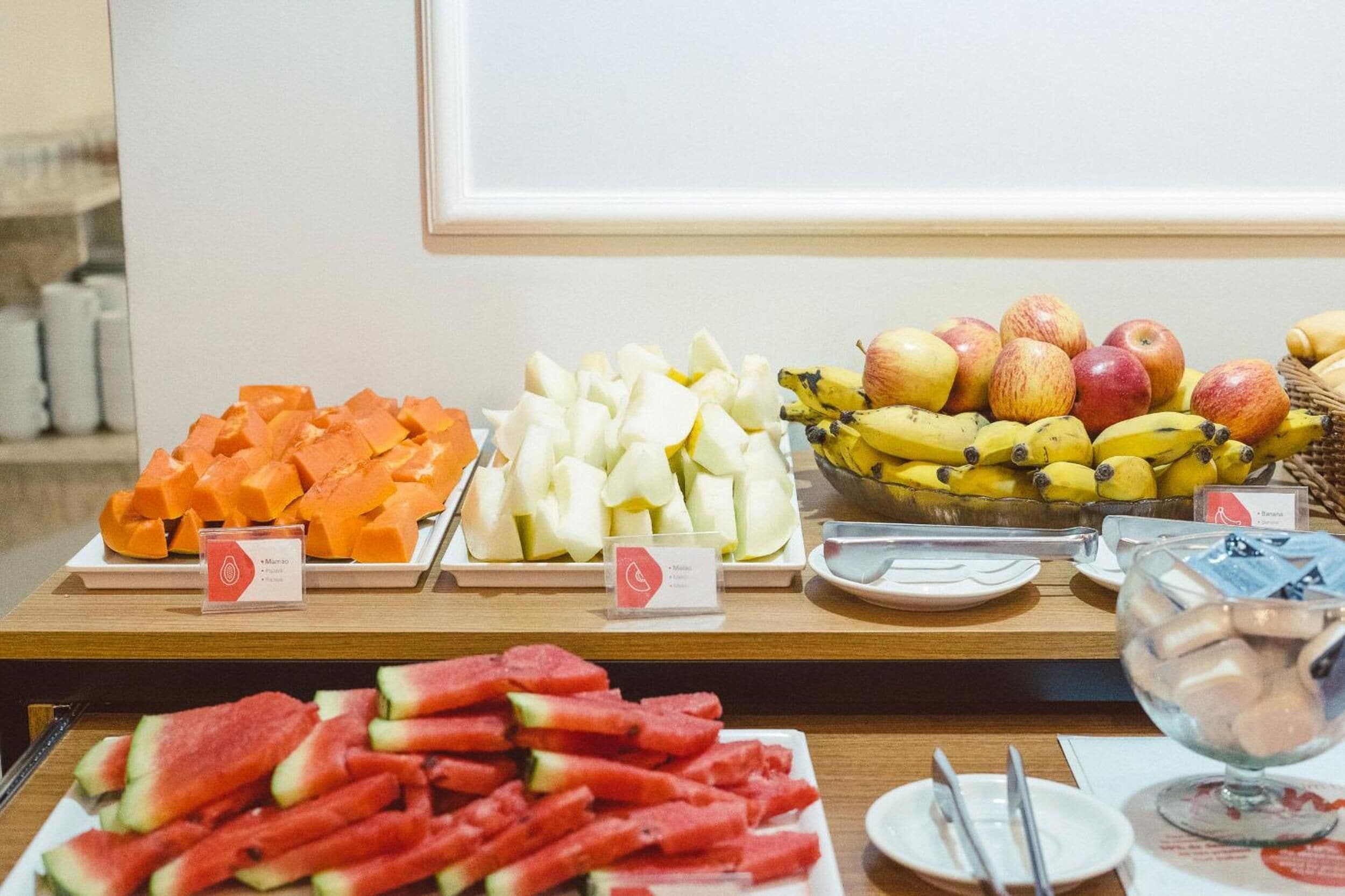 A buffet table with various fruits and vegetables, including watermelon, apples, bananas, and carrots.