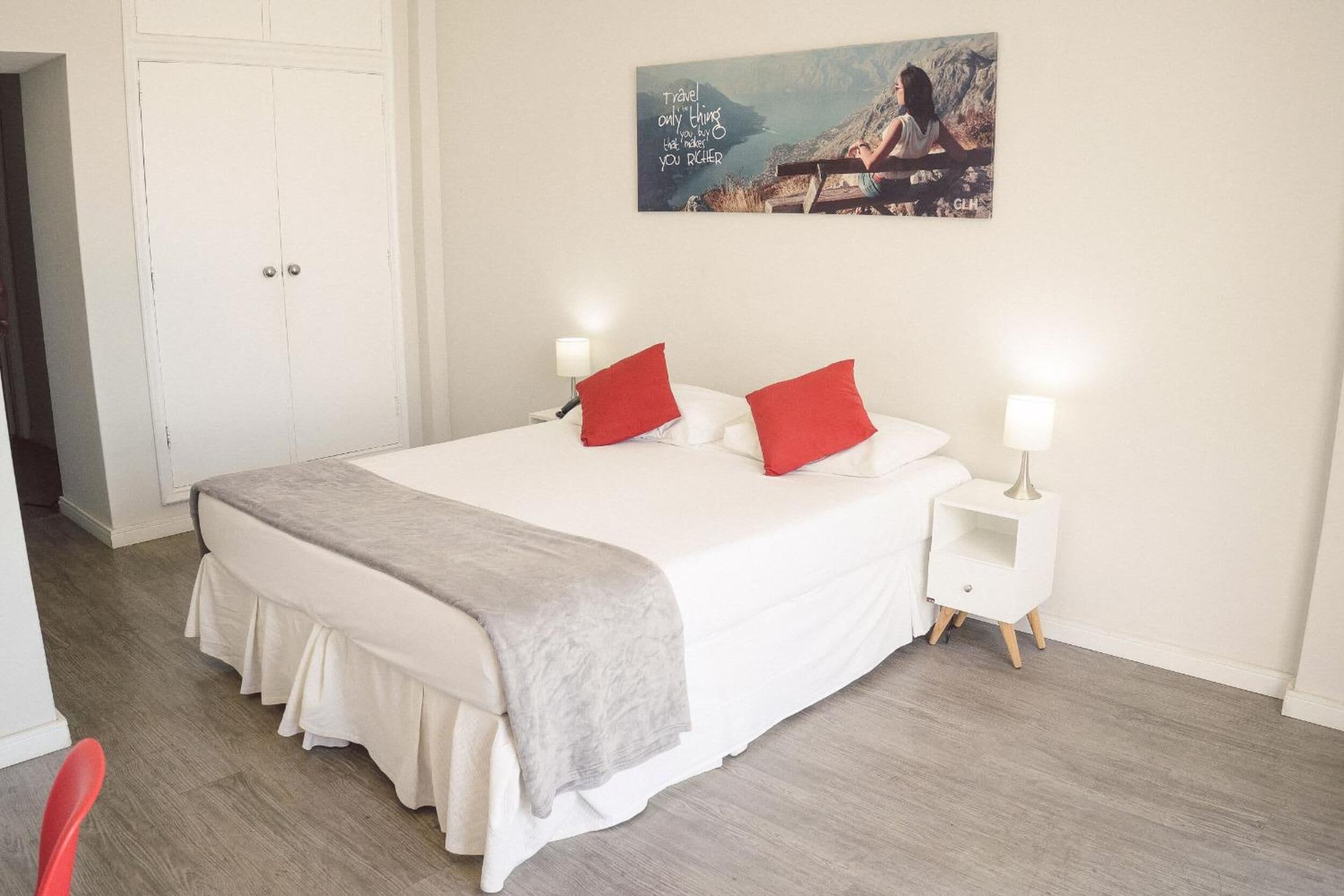 A neatly arranged bedroom with a large bed, two bedside tables with lamps, a door, and a wall-mounted painting.
