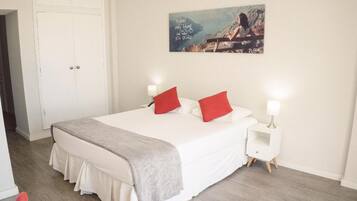 A neatly arranged bedroom with a large bed, two bedside tables with lamps, a door, and a wall-mounted painting.