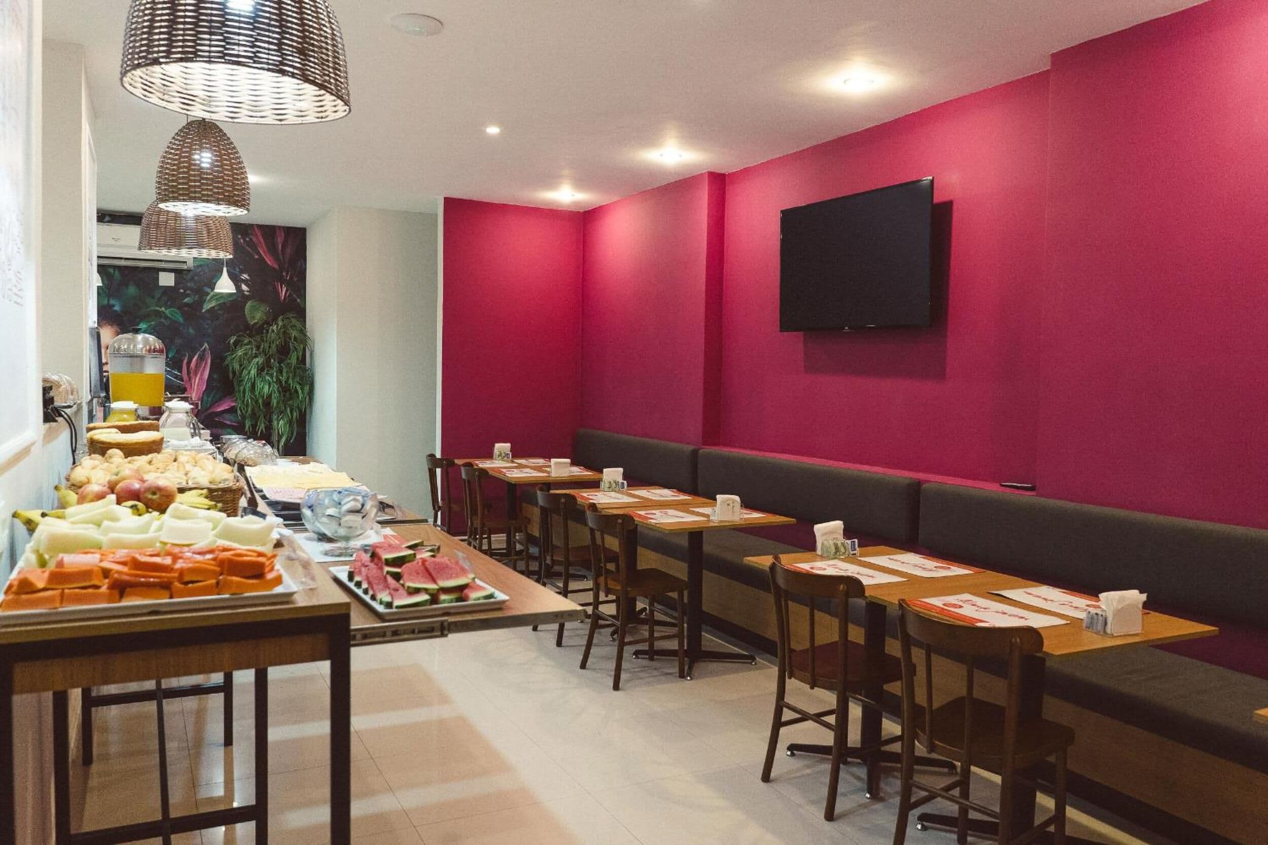 A dining area with multiple tables, benches, and a flat-screen TV mounted on the wall.