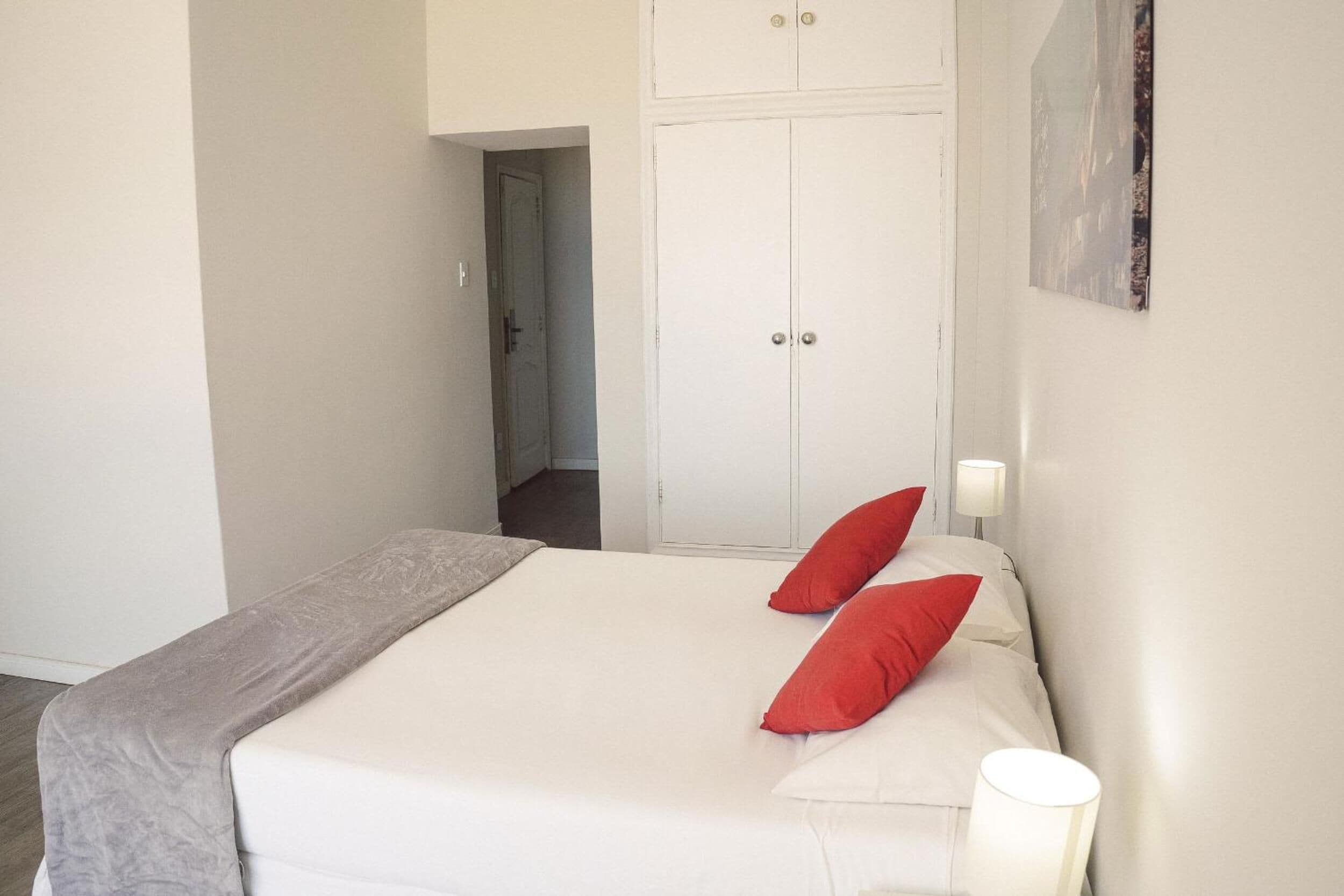 A bedroom with a bed, two red pillows, a bedside lamp, and a wardrobe.