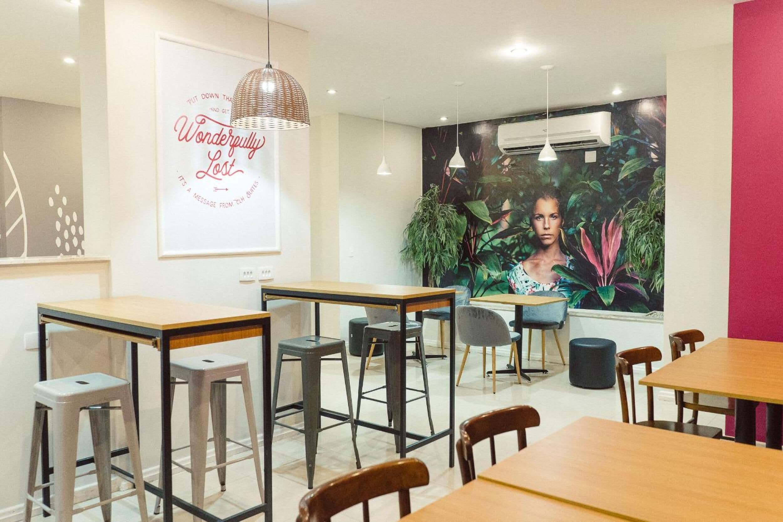 Um café moderno com mesas e banquetas de madeira, um grande mural de uma mulher e um aparelho de ar condicionado na parede.