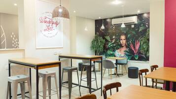 Um café moderno com mesas e banquetas de madeira, um grande mural de uma mulher e um aparelho de ar condicionado na parede.